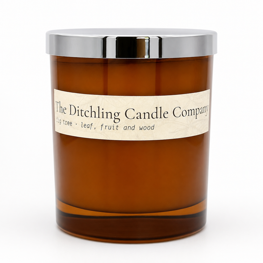 Amber glass fig tree scented soy candle by The Ditchling Candle Company with a silver lid, shown on a clean white background.