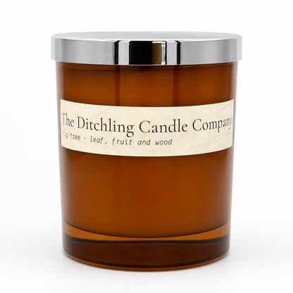 Amber glass fig tree scented soy candle by The Ditchling Candle Company with a silver lid, shown on a clean white background.