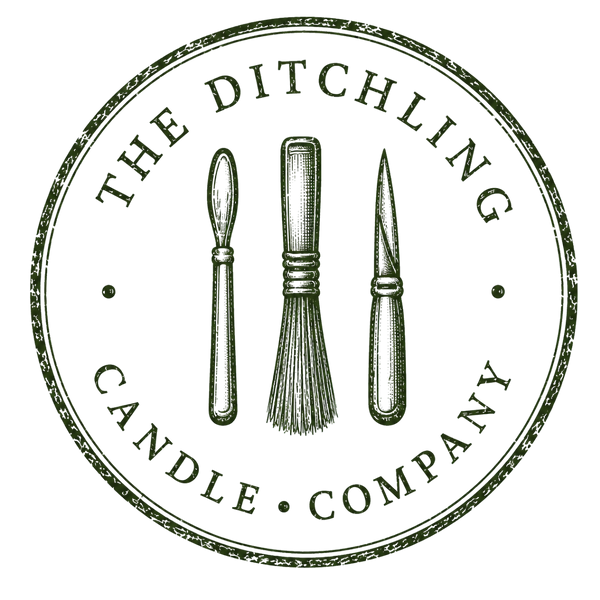 A circular vintage-style logo for The Ditchling Candle Company, featuring three candle-making tools—a spoon, a brush, and a knife—centered within a distressed round border on a white background.