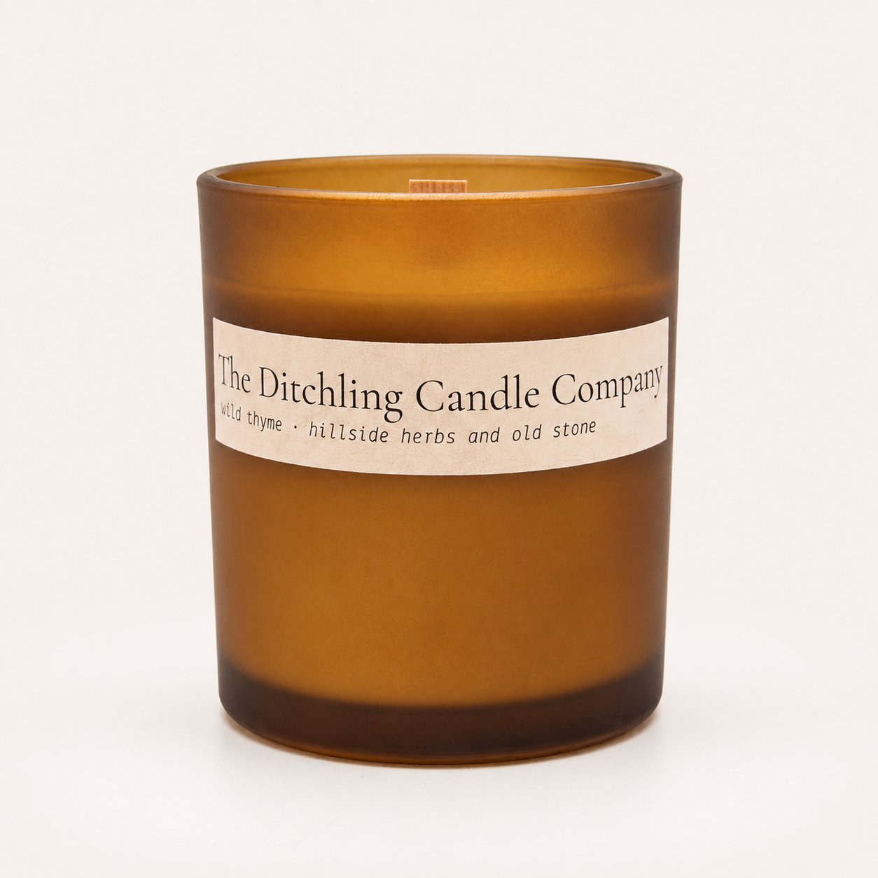 Amber glass wild thyme scented soy candle by The Ditchling Candle Company with a wooden wick, shown open on a warm off-white background.